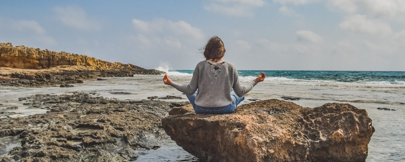 Woman meditating by the ocean on a stone