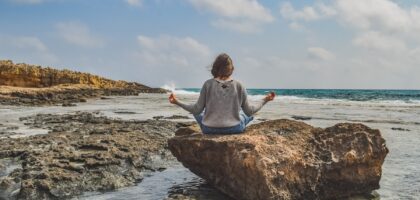 Woman meditating by the ocean on a stone